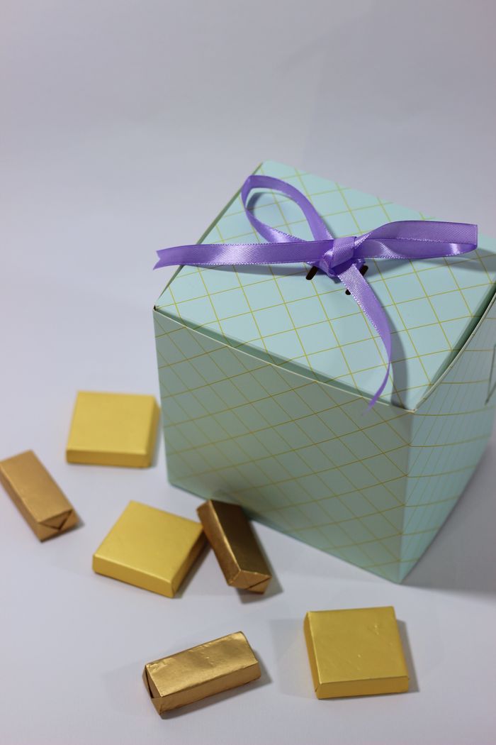 Services A stylish gift box tied with a purple ribbon, surrounded by gold-wrapped chocolates, perfect for celebrations.