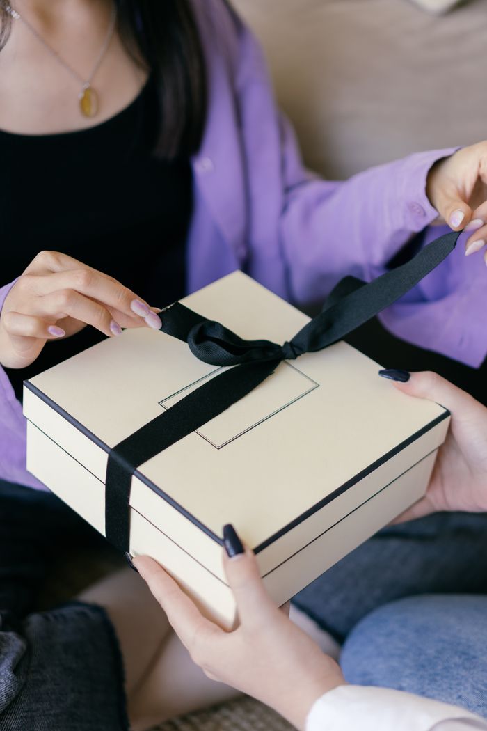 Close-up of a woman unwrapping a decorated gift box indoors.